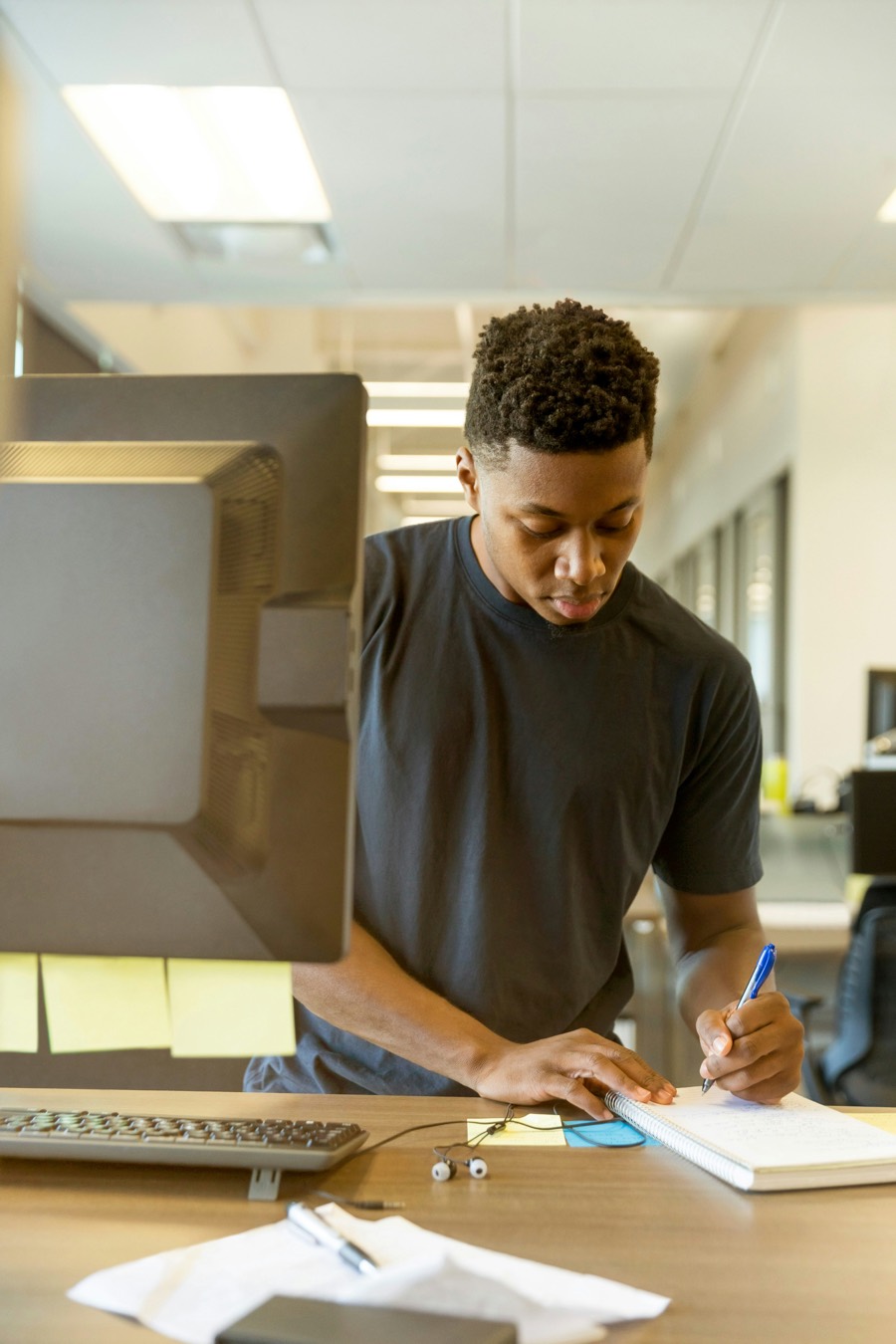 A sales professional standing at a desk, taking notes beside a computer while working through customer enquiries.